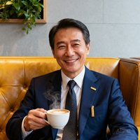 一位身着深蓝色西装、佩戴金色领带夹的中年商务旅客陈先生，面带微笑坐在贵宾休息室的皮质沙发上，手中拿着一杯现磨咖啡